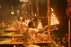 Priests dressed in traditional attire performing the Ganga Aarti at Dashashwamedh Ghat in Varanasi, India. The priests hold multi-tiered brass lamps with flames, creating a mesmerizing glow against the night sky.