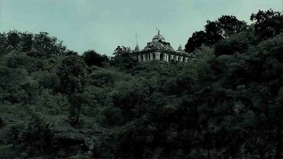 A historic fort perched on a hilltop, surrounded by lush green trees. The fort appears ancient and majestic.
