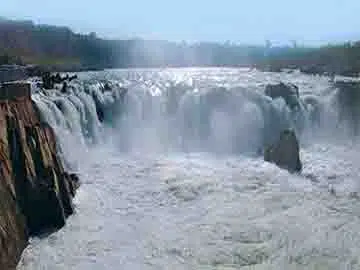 The majestic Dhuandhar Falls cascading down a rocky cliff, surrounded by lush greenery.