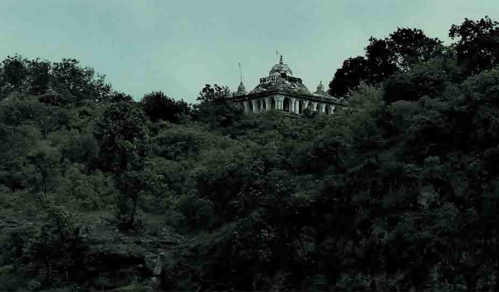 A historic fort perched on a hilltop, surrounded by lush green trees. The fort appears ancient and majestic.